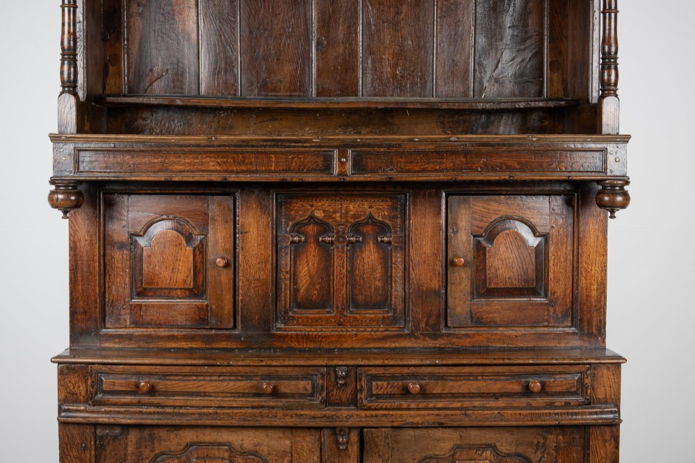 A dark oak three-tier Welsh cwpwrdd tridarn featuring an open upper canopy, middle cupboard section with raised arch panels and turned pillars, and a base cupboard with two drawers. View IX