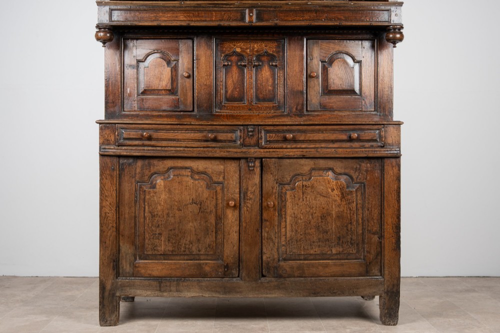 A dark oak three-tier Welsh cwpwrdd tridarn featuring an open upper canopy, middle cupboard section with raised arch panels and turned pillars, and a base cupboard with two drawers. View X