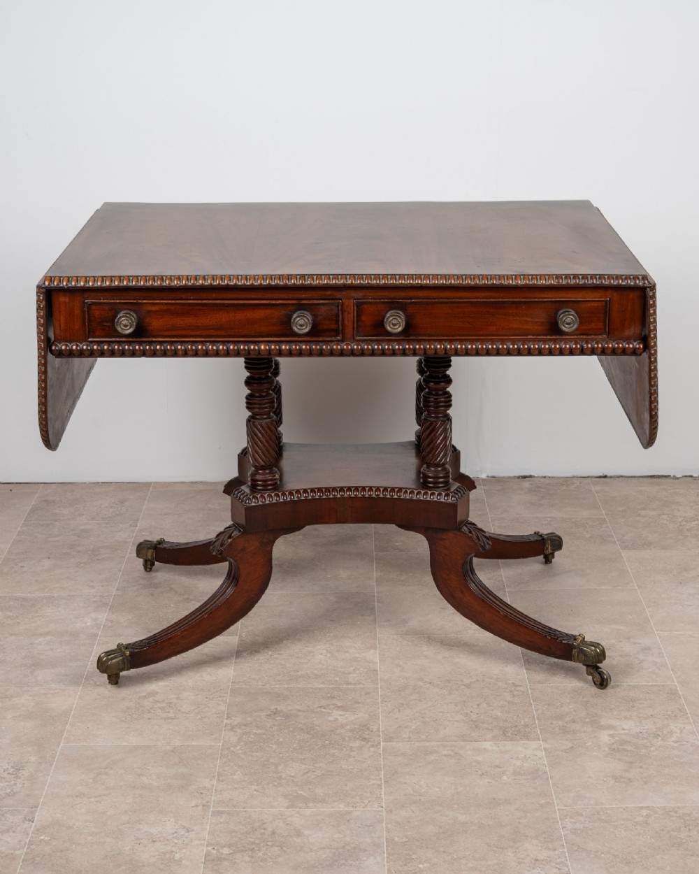 An antique Regency mahogany drop-leaf sofa table with two drawers, spiral-turned column supports, and splayed legs on brass castors. View II