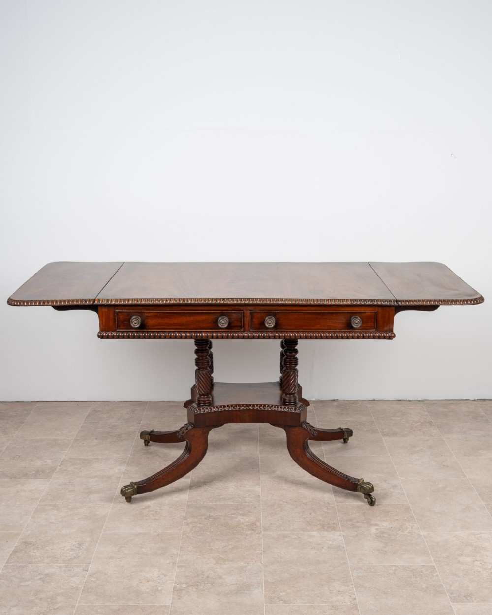 An antique Regency mahogany drop-leaf sofa table with two drawers, spiral-turned column supports, and splayed legs on brass castors. View III