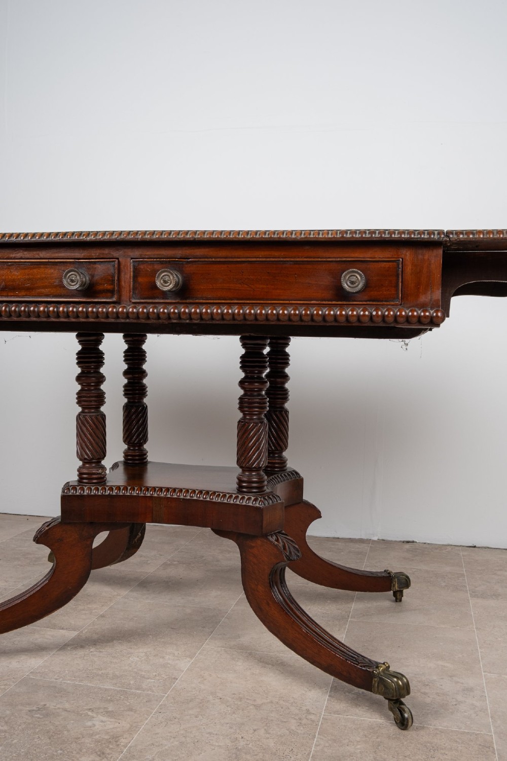 An antique Regency mahogany drop-leaf sofa table with two drawers, spiral-turned column supports, and splayed legs on brass castors. View IV