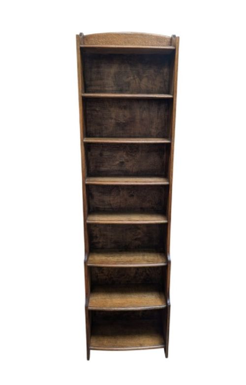 A tall, narrow warm brown oak open bookcase featuring graduated waterfall sides and seven tiers of shelving. View VII