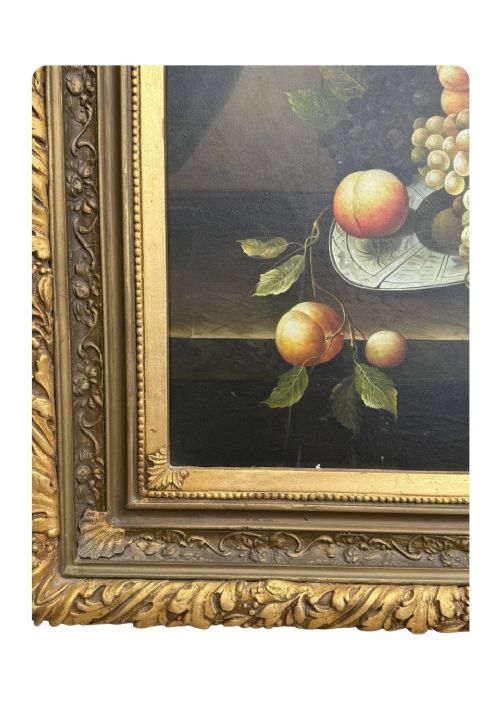 An antique oil painting depicting a detailed still life of grapes and peaches on a dark background, set within an ornate carved giltwood frame. View V