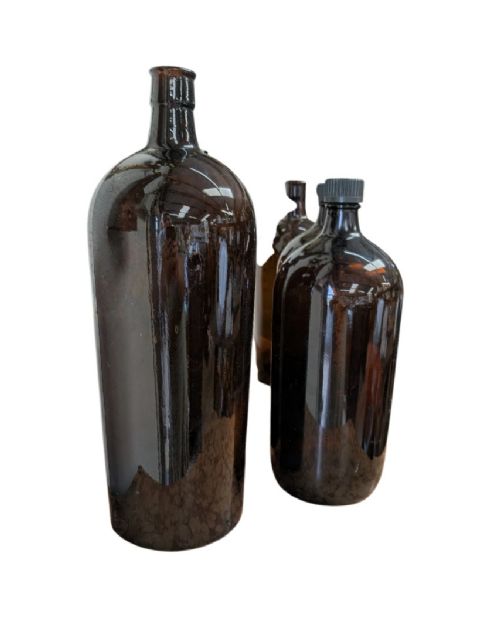 A set of six cylindrical amber glass Winchester apothecary bottles with narrow necks and black screw caps against a white background. View II
