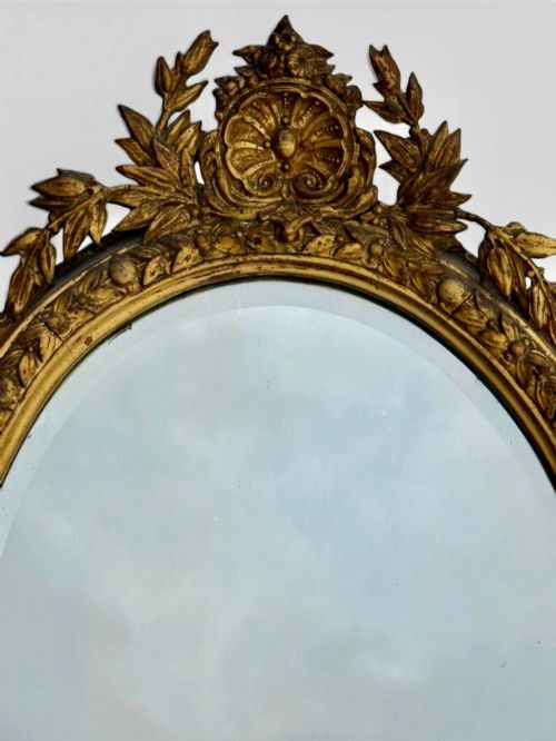 fig 1. An oval Victorian giltwood and gesso girandole wall mirror featuring floral cresting, a beaded inner rim, and a three-branch candle sconce at the base.