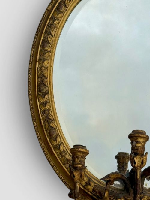 fig 2. An oval Victorian giltwood and gesso girandole wall mirror featuring floral cresting, a beaded inner rim, and a three-branch candle sconce at the base.