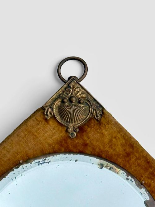 fig 4. A diamond-shaped wall mirror featuring a mustard yellow velvet frame with decorative brass corner mounts, a central round bevelled glass mirror, and an integrated brass candle sconce at the lower vertex.