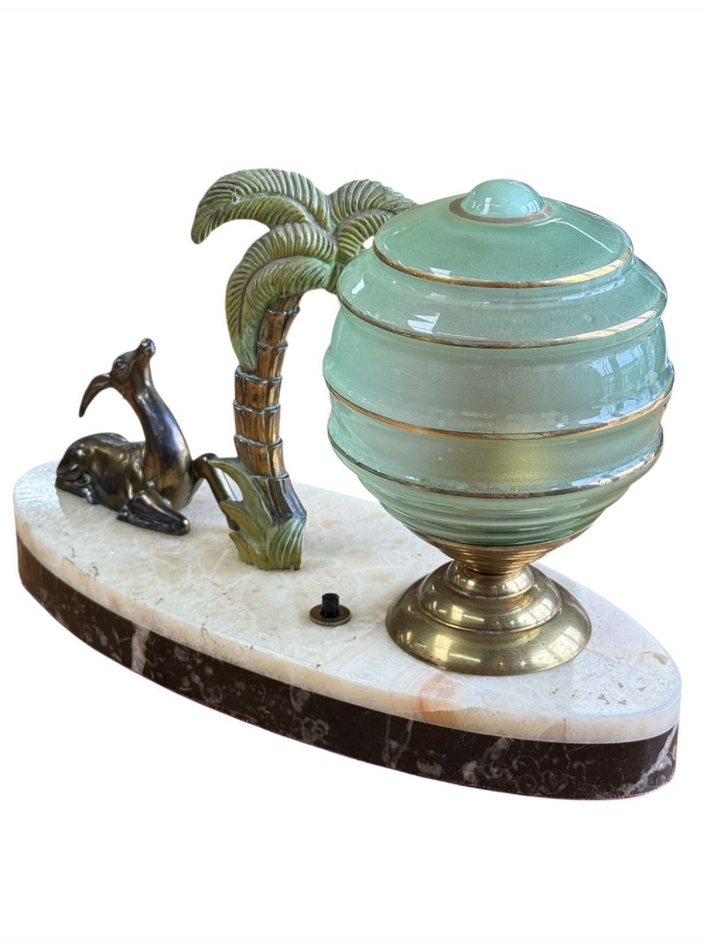 An Art Deco table lamp with a green stepped glass shade, metal palm tree, and reclining gazelle figure on an oval white marble base. View II
