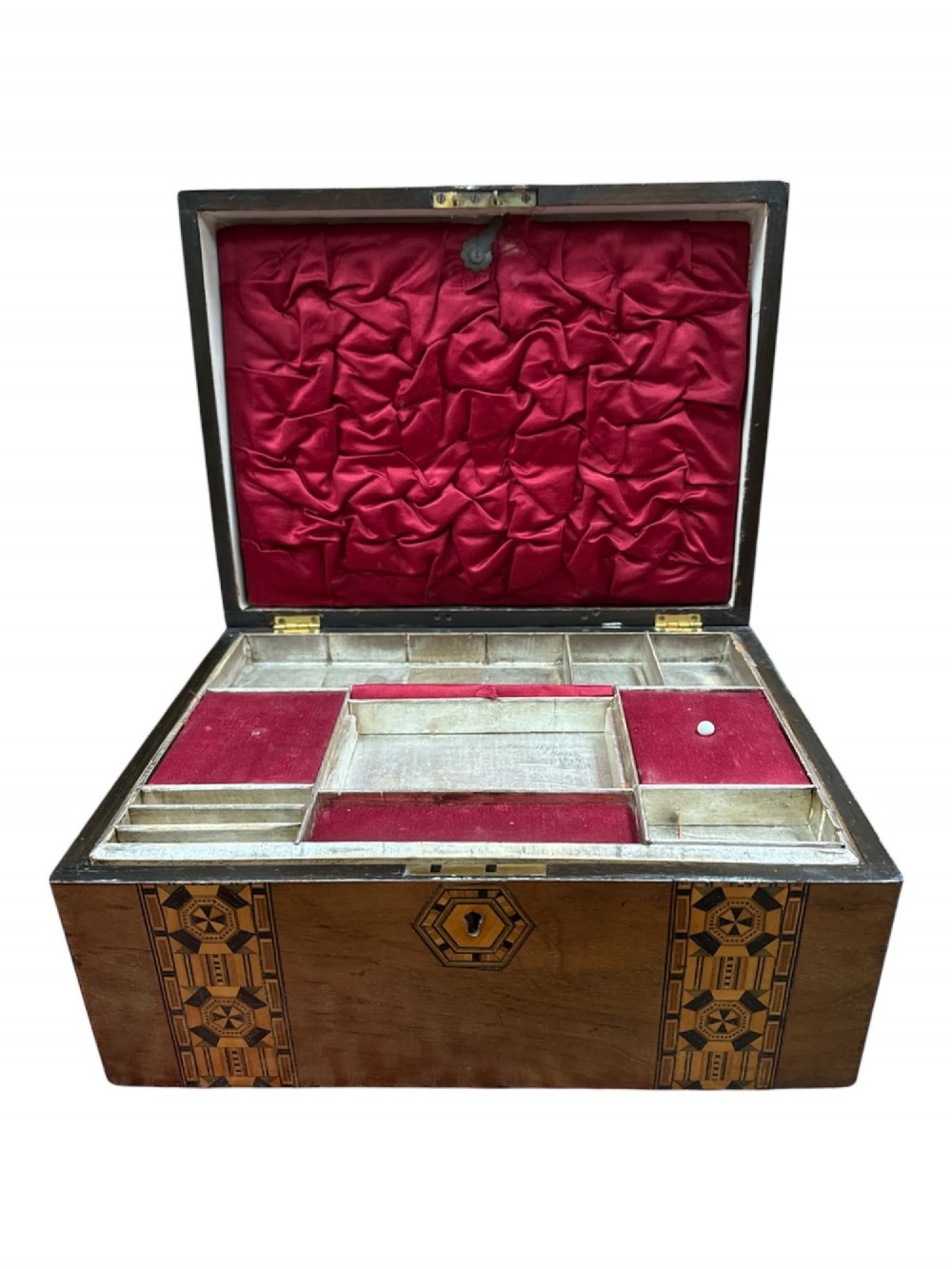 An open antique Victorian wooden sewing box featuring geometric Tunbridge ware mosaic inlay and a red ruched silk interior with removable tray compartments.