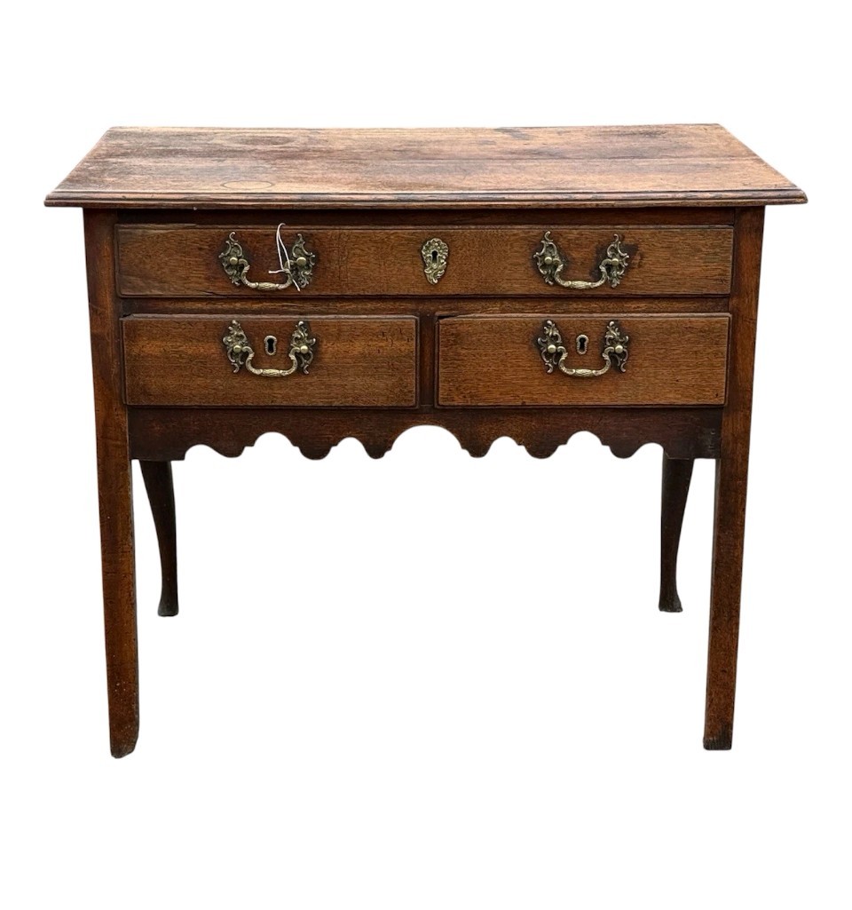 An 18th-century Georgian oak lowboy table featuring one wide upper drawer, two lower drawers, decorative brass handles, and a shaped apron.