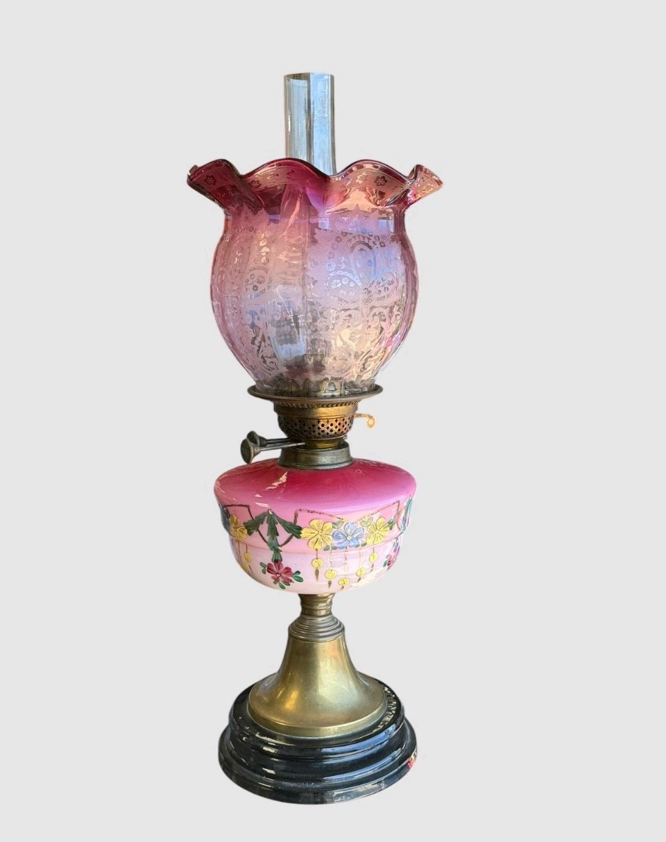 A Victorian cranberry glass oil lamp with a ruffled etched shade, hand-painted floral reservoir, brass burner, and stepped black base. View IV