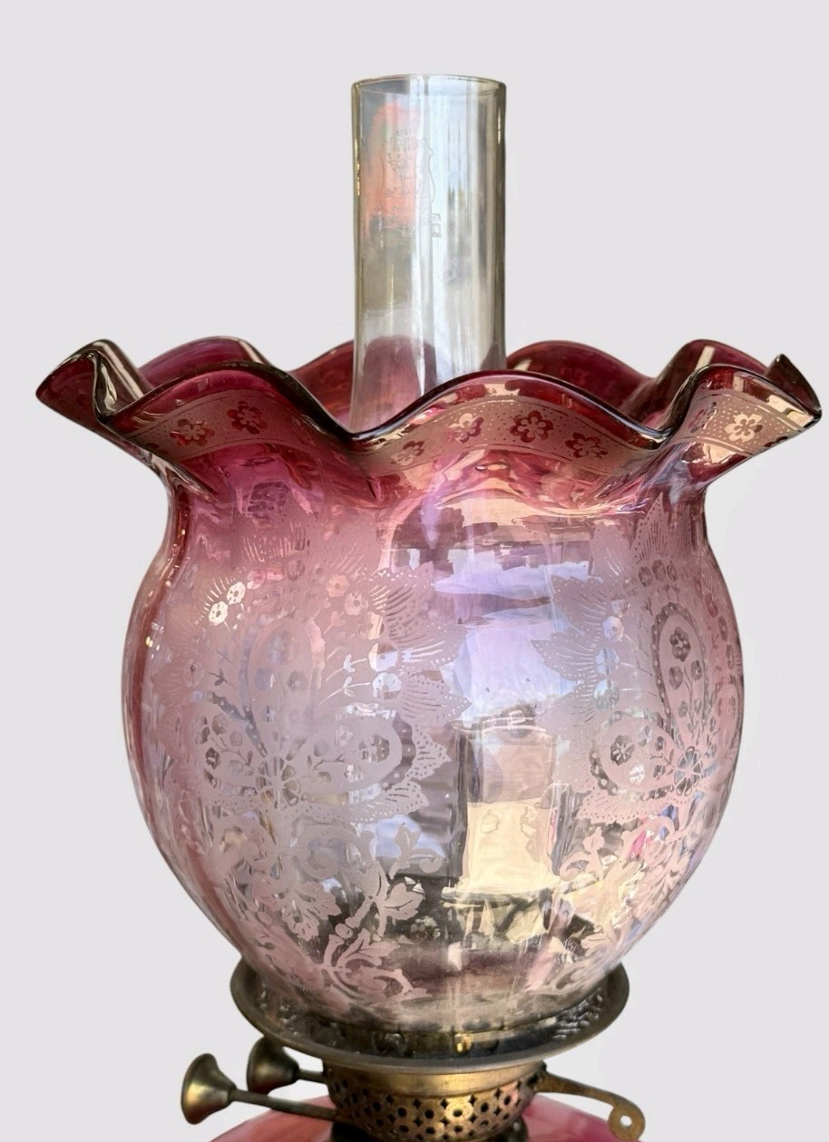 A Victorian cranberry glass oil lamp with a ruffled etched shade, hand-painted floral reservoir, brass burner, and stepped black base. View IX