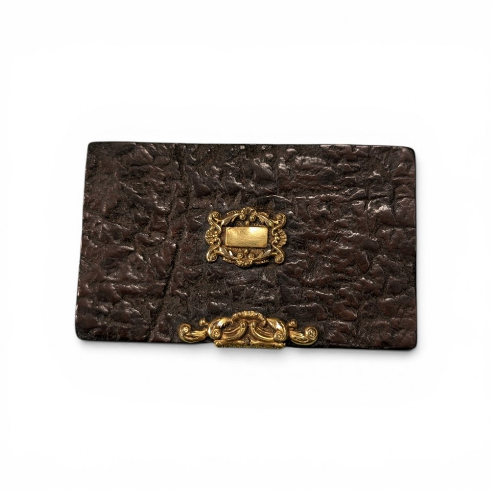 A rectangular 19th-century dark brown rhinoceros hide snuff box featuring an ornate gilt metal central cartouche and matching clasp.
