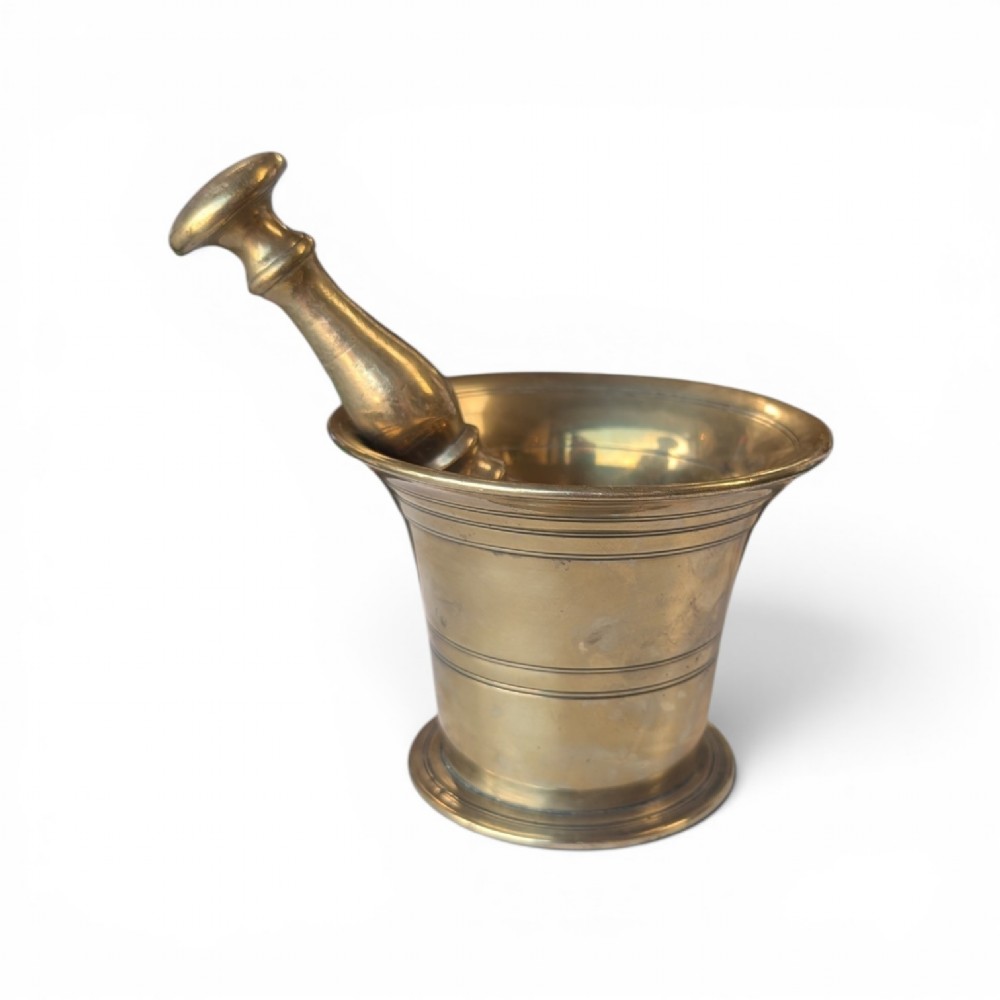 A cast brass mortar with a flared upper rim and incised lines, shown alongside a turned brass pestle.
