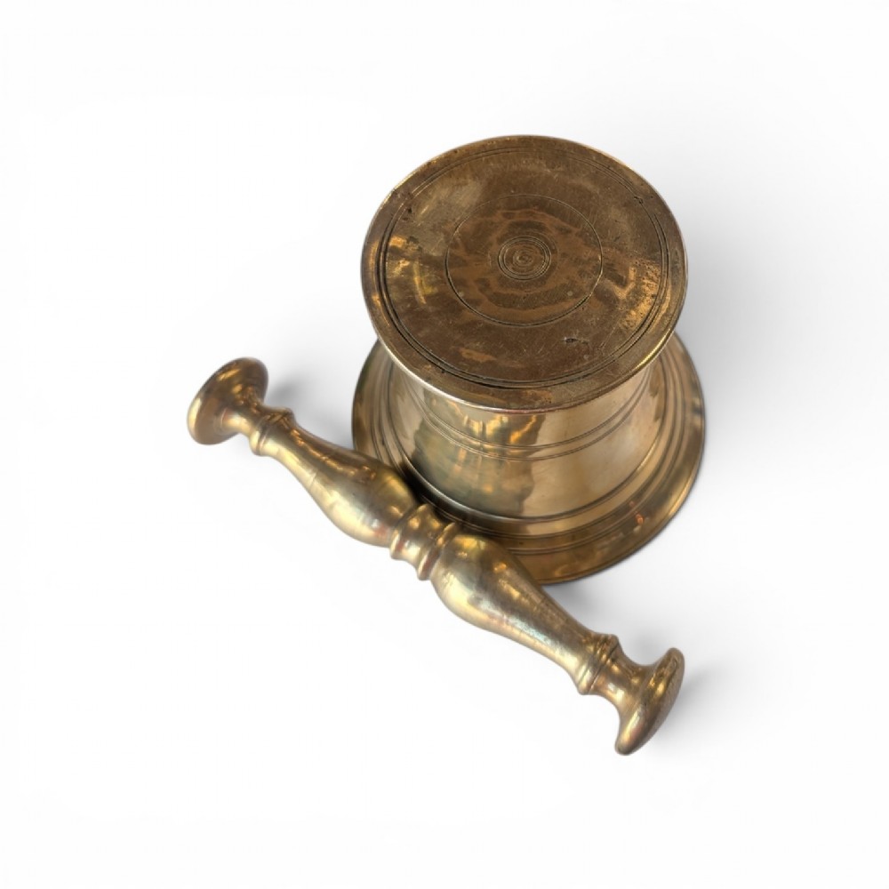 A cast brass mortar with a flared upper rim and incised lines, shown alongside a turned brass pestle. View V