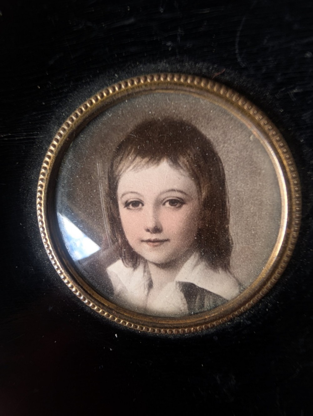 A square wooden frame featuring a dark ebonised circular surround with gilt corner decorations and an inset portrait of a child. View IV