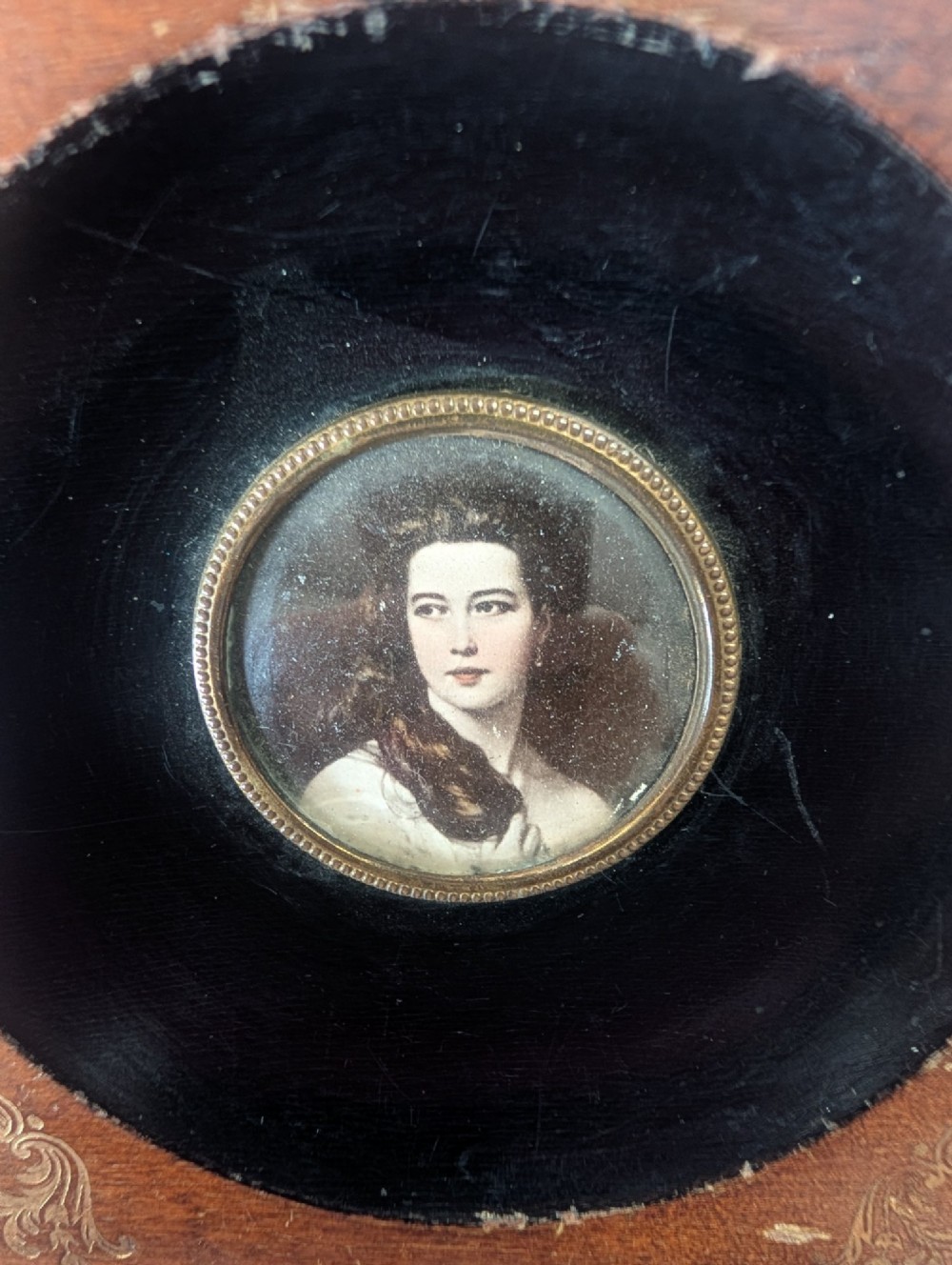A square wooden frame featuring a dark ebonised circular surround with gilt corner decorations and an inset portrait of a child. View VIII