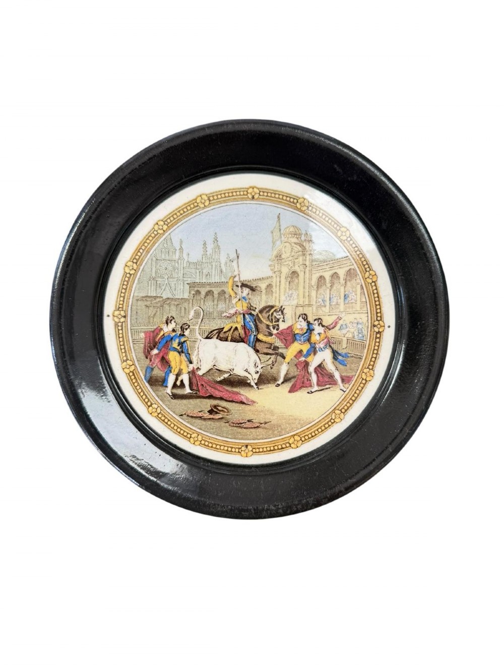 A circular ceramic plate depicting a transfer-printed bullfighting scene, framed within a wide circular black ebonised surround.