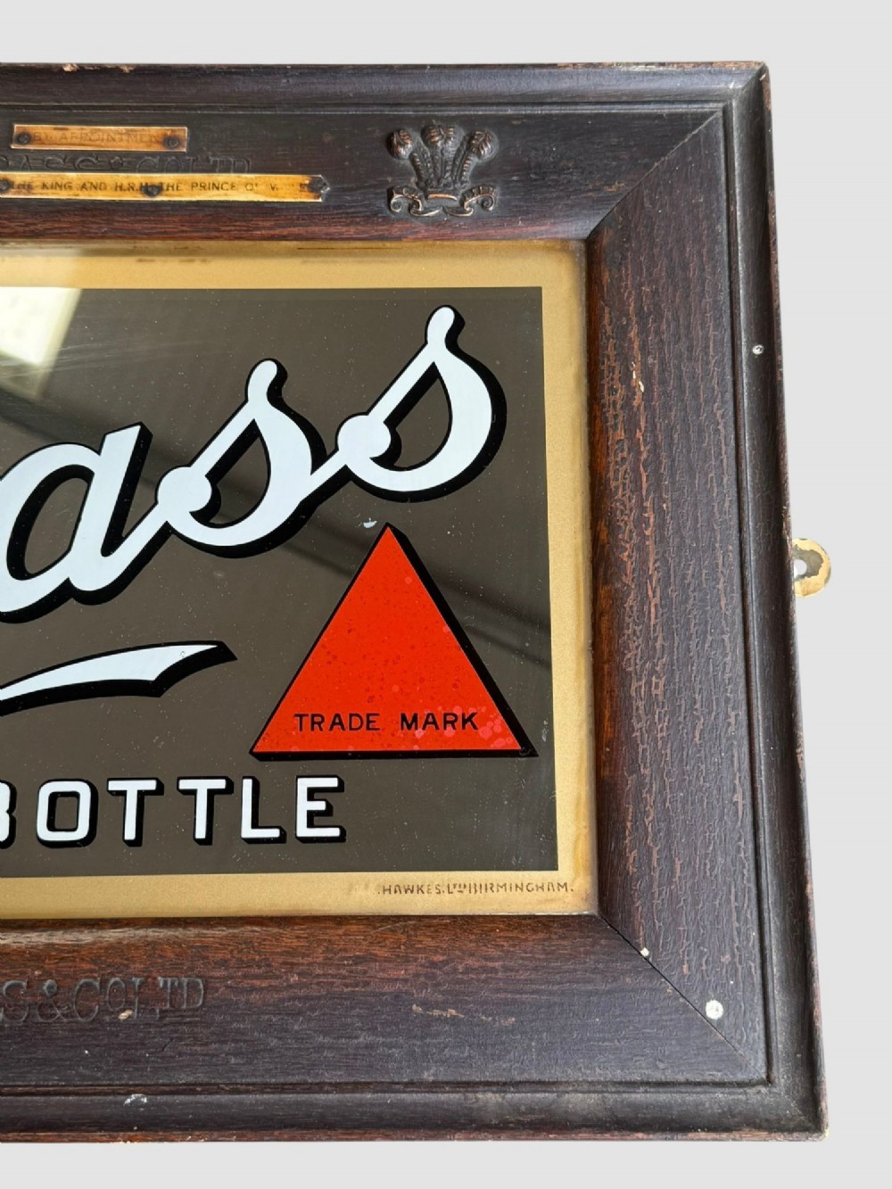 An antique dark oak framed advertising mirror featuring white script reading Bass in Bottle alongside a red triangle logo and brass Royal Warrant badges. View VI