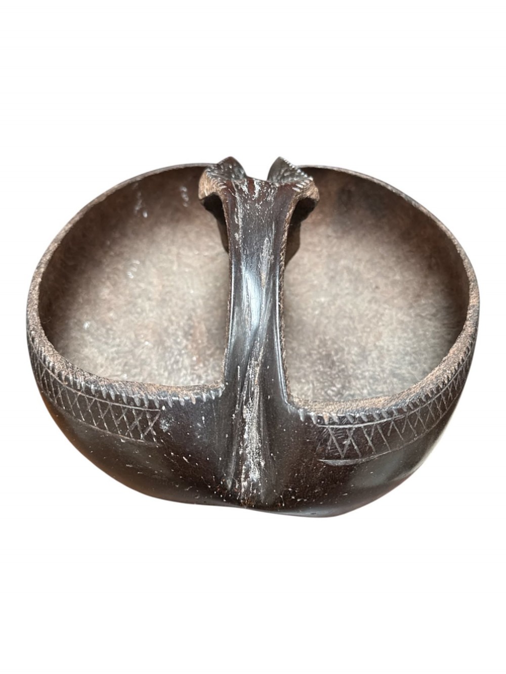 A dark brown carved Coco de Mer nut shell fashioned into a basket vessel with a central handle and incised geometric rim detailing.