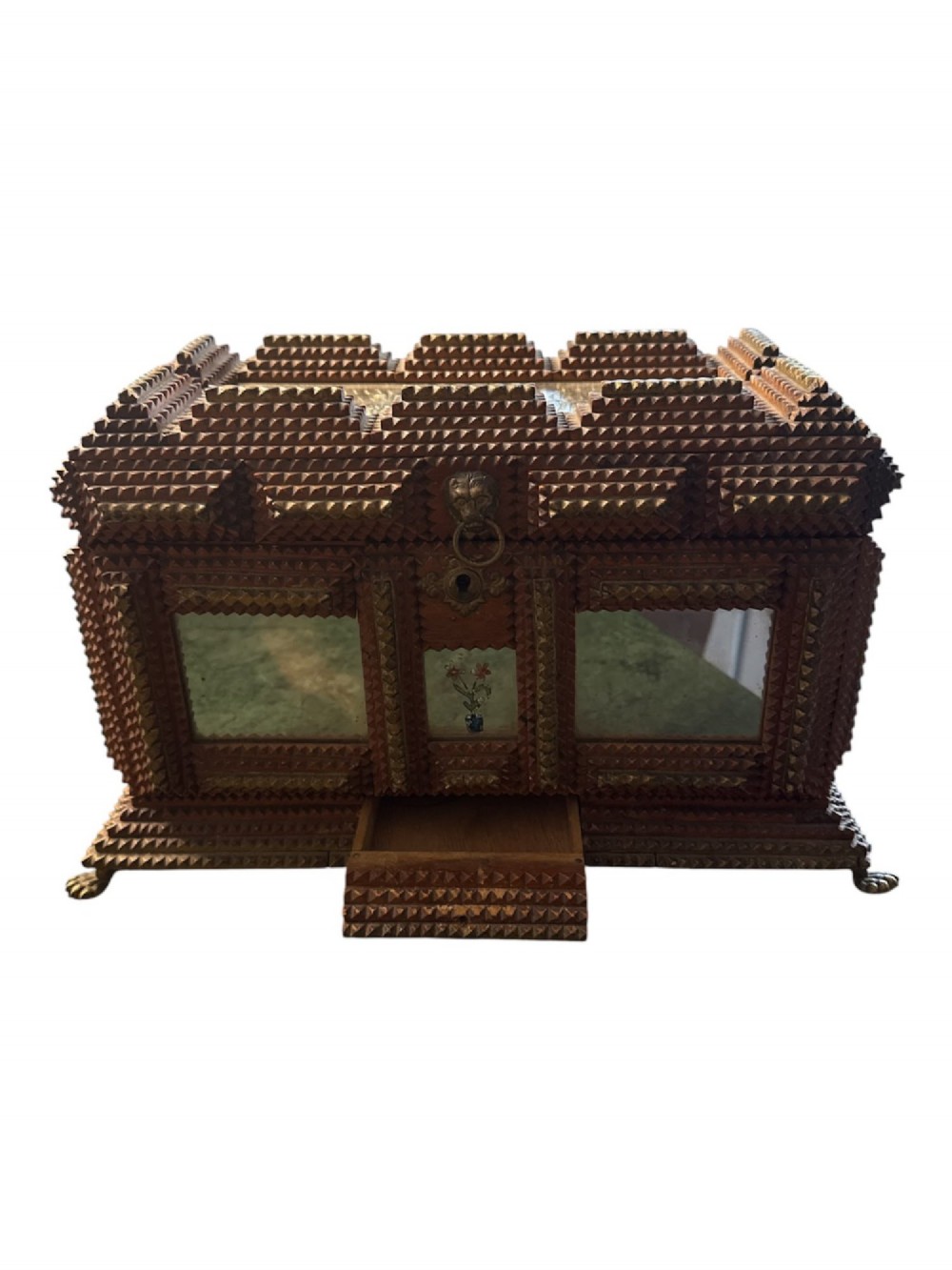 A Victorian tramp art wooden box featuring chip-carved pyramid layers, glass inserts, a metal lion head pull, and small metal feet.