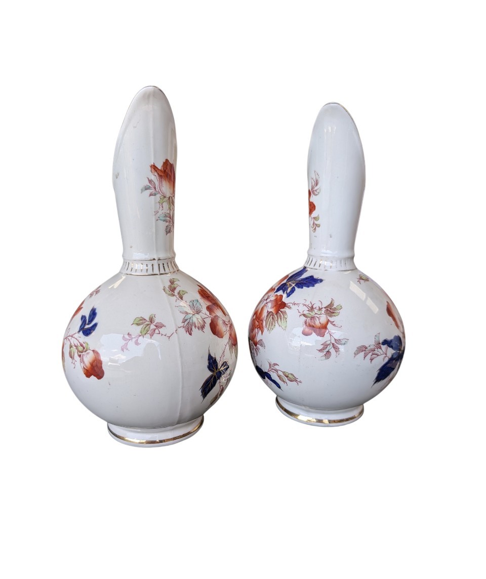 A pair of antique Japanese Imari porcelain pitchers featuring rounded bodies, tall swept spouts, dark blue handles, and hand-painted rust red flowers with gilded accents. View III