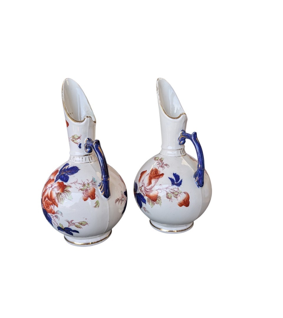 A pair of antique Japanese Imari porcelain pitchers featuring rounded bodies, tall swept spouts, dark blue handles, and hand-painted rust red flowers with gilded accents. View IV