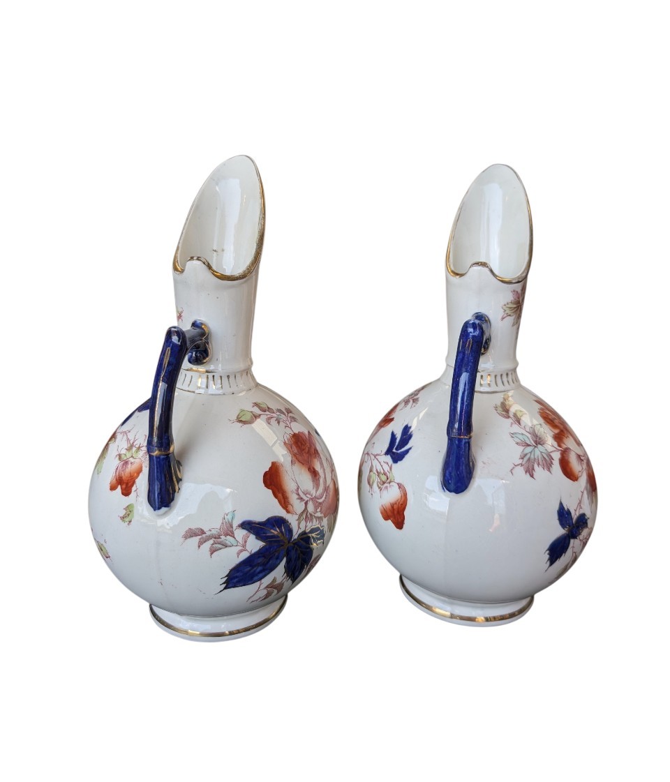 A pair of antique Japanese Imari porcelain pitchers featuring rounded bodies, tall swept spouts, dark blue handles, and hand-painted rust red flowers with gilded accents. View VIII