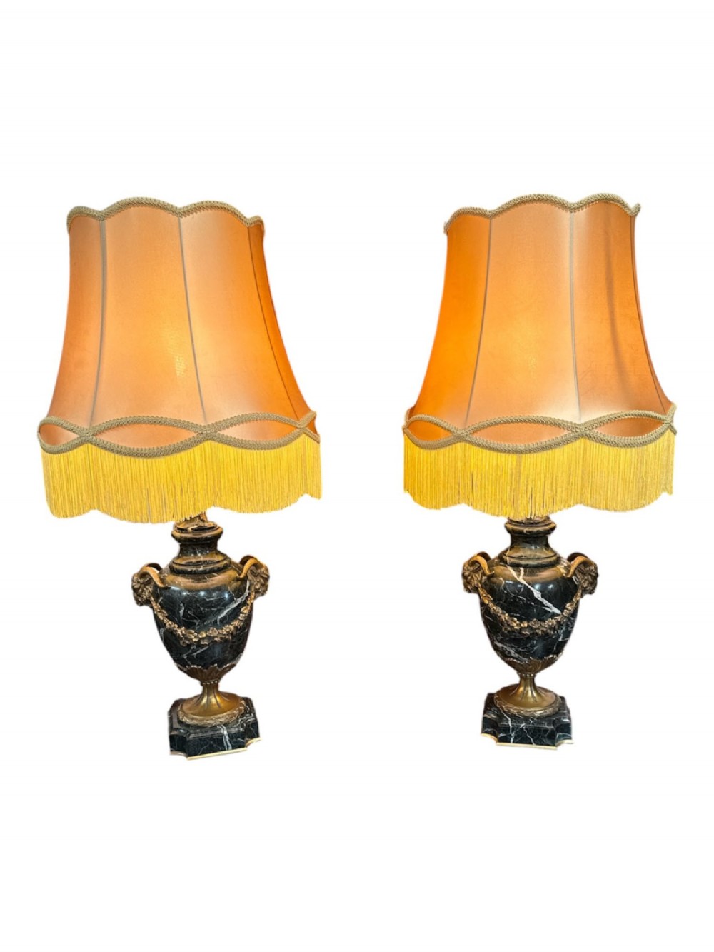 A pair of 19th-century French table lamps crafted from dark veined marble in urn shapes with gilt metal mounts and amber fabric shades featuring fringe trim.