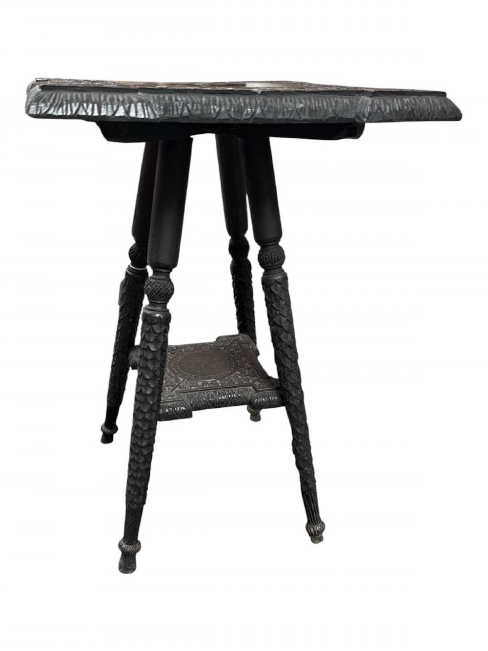 A 19th-century dark hardwood Anglo-Indian occasional table featuring intricately carved scale motifs on the legs, a carved undertier shelf, and a textured top.