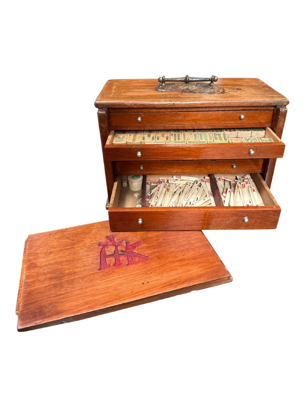 An antique warm brown wooden cabinet featuring a metal top handle, a removable front panel with red characters, and multiple drawers holding mahjong tiles and counting sticks.
