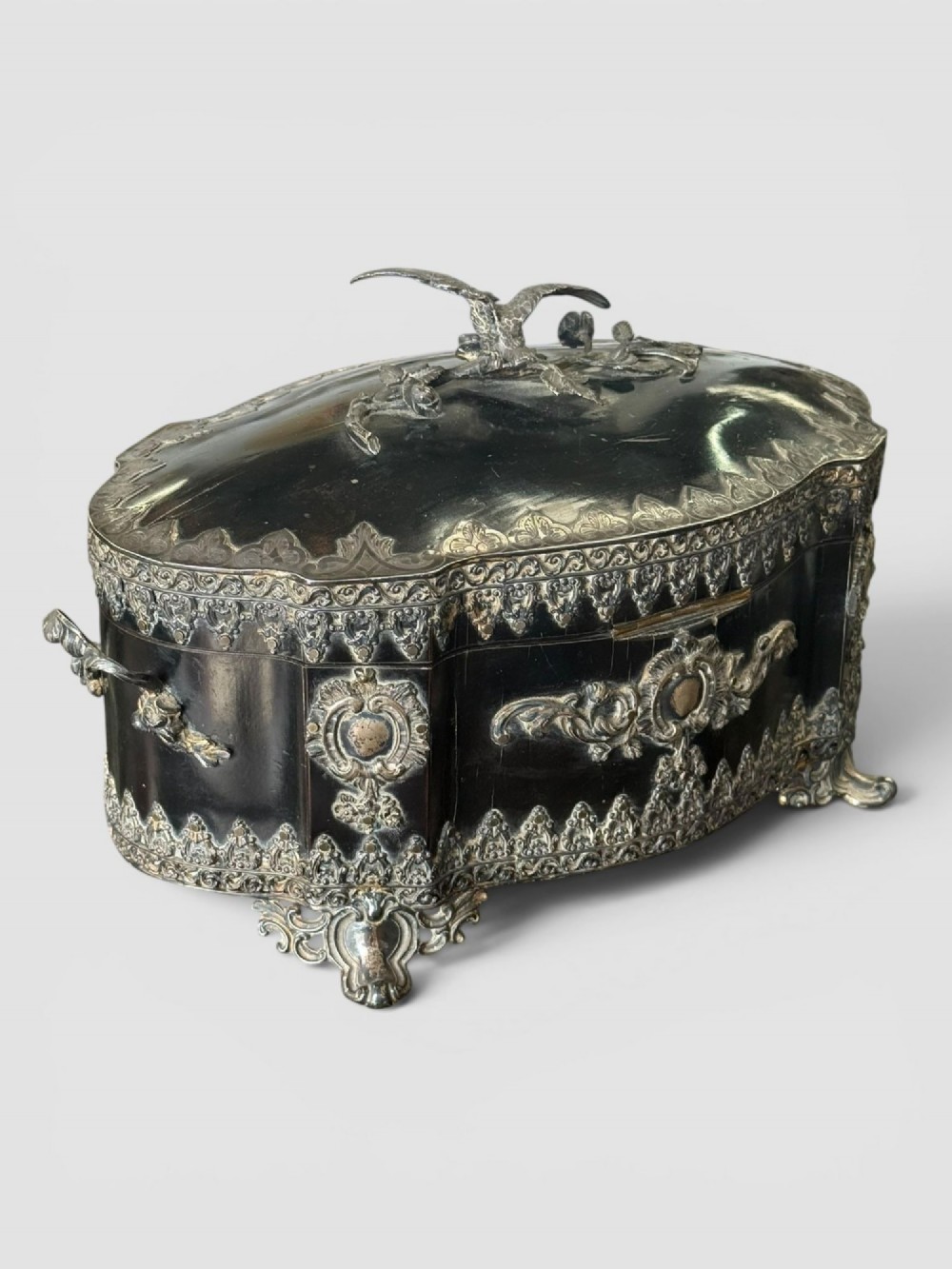 A 19th-century French ebonised serpentine table casket featuring elaborate silvered metal scrollwork mounts, raised feet, and a lid top decorated with a winged bird finial. View II