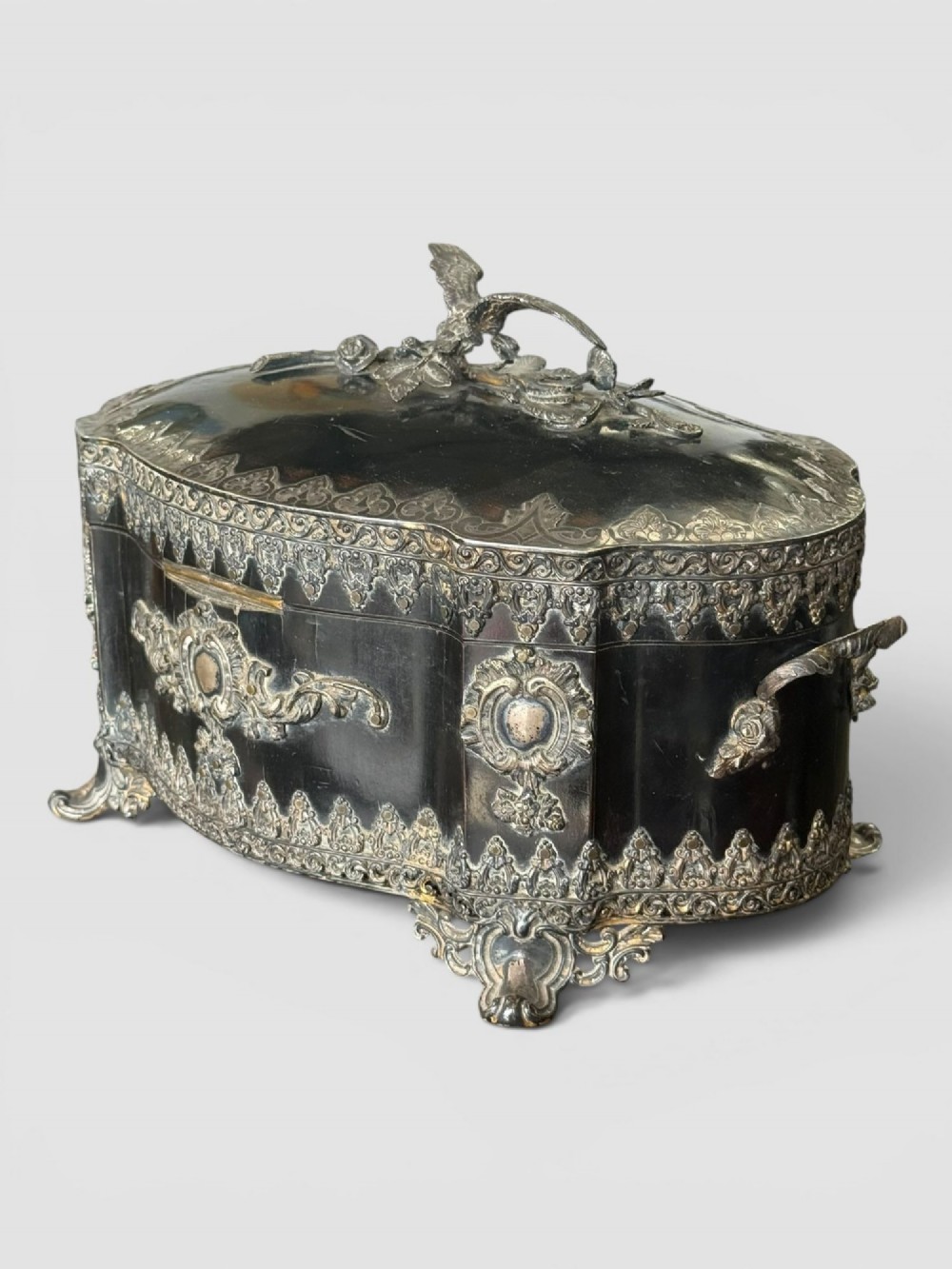 A 19th-century French ebonised serpentine table casket featuring elaborate silvered metal scrollwork mounts, raised feet, and a lid top decorated with a winged bird finial. View III