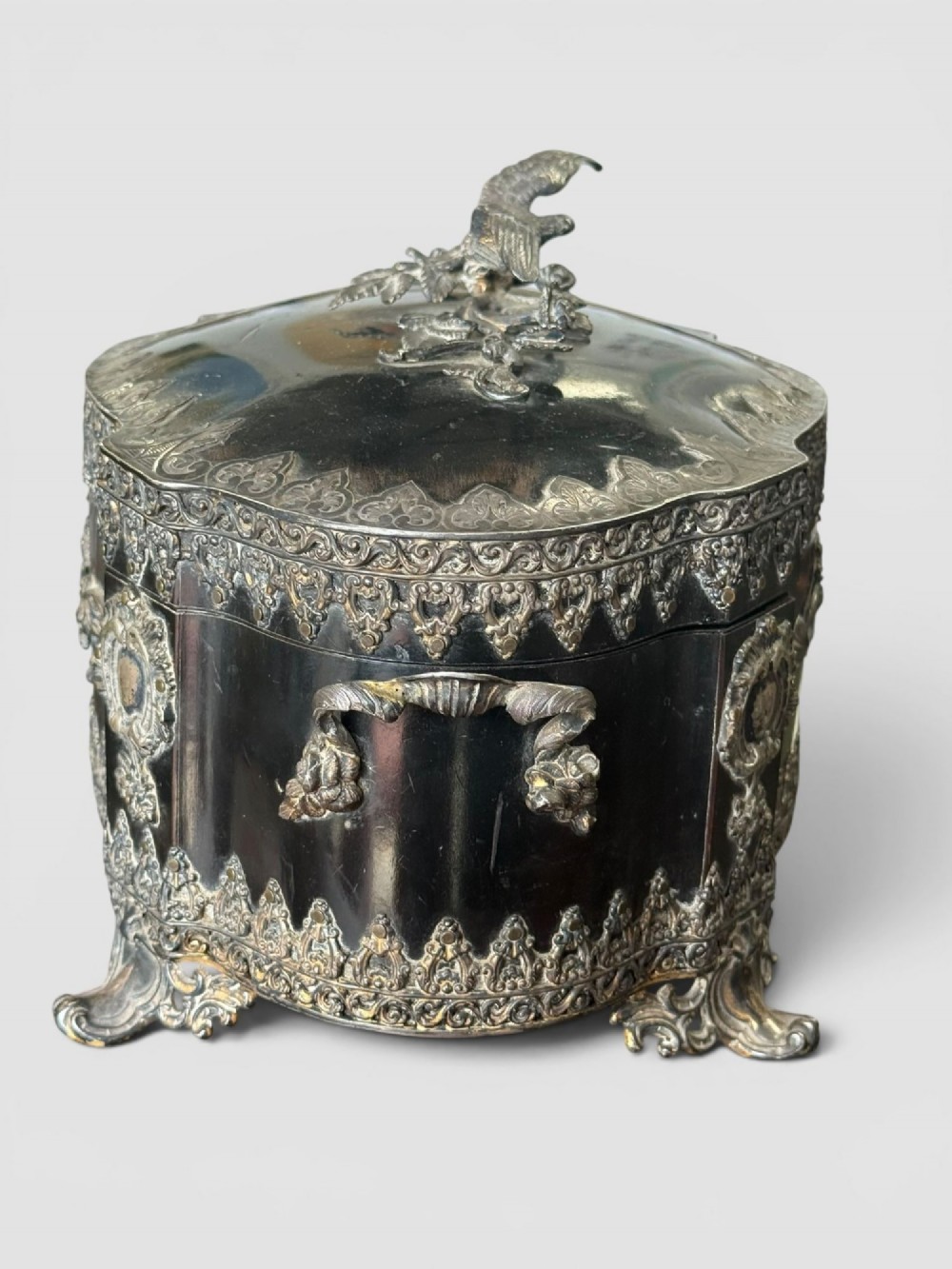 A 19th-century French ebonised serpentine table casket featuring elaborate silvered metal scrollwork mounts, raised feet, and a lid top decorated with a winged bird finial. View IV