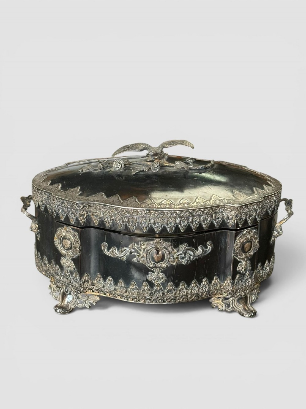 A 19th-century French ebonised serpentine table casket featuring elaborate silvered metal scrollwork mounts, raised feet, and a lid top decorated with a winged bird finial. View V