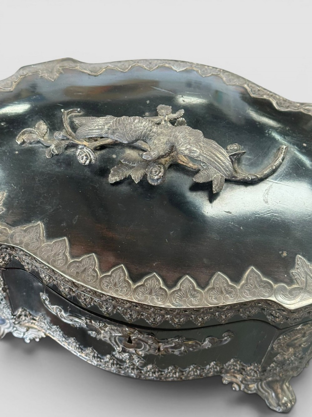 A 19th-century French ebonised serpentine table casket featuring elaborate silvered metal scrollwork mounts, raised feet, and a lid top decorated with a winged bird finial. View VII