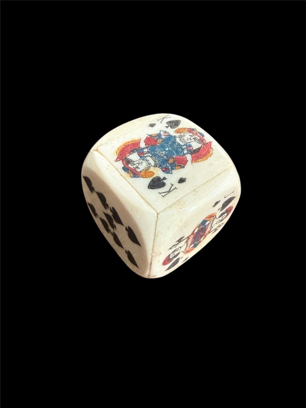A cream-coloured carved bone poker die decorated with hand-coloured playing card suits and figures on each face.