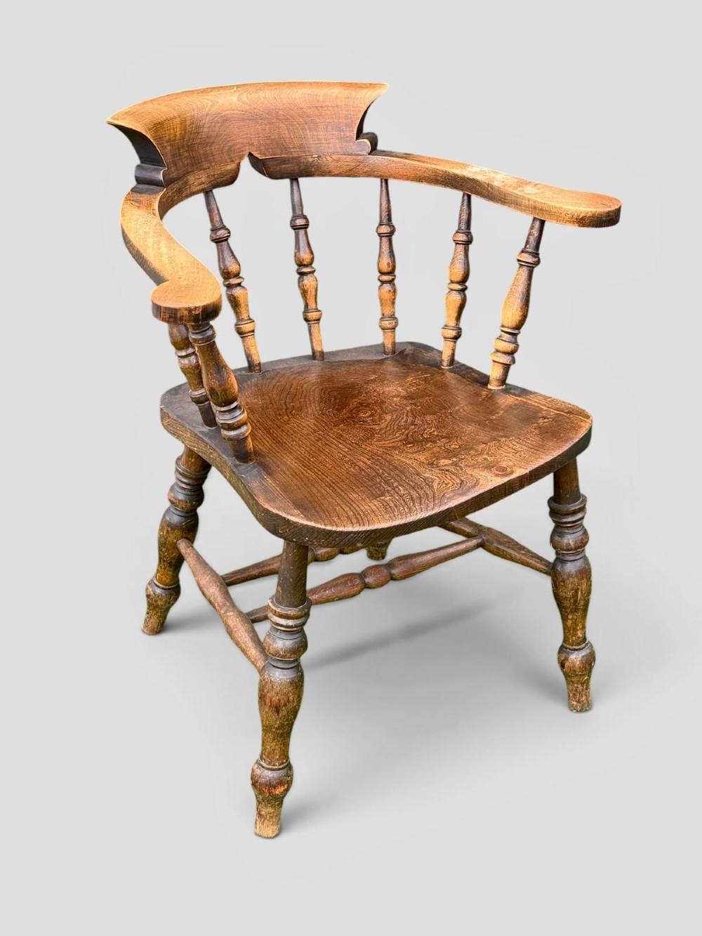 An antique Victorian beech and elm smokers captains chair with turned spindles, a contoured saddle seat, and turned legs. View II