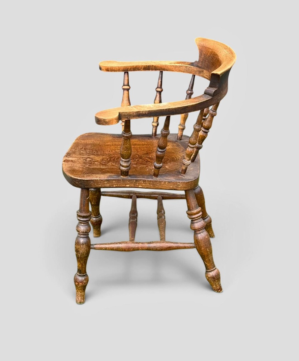 An antique Victorian beech and elm smokers captains chair with turned spindles, a contoured saddle seat, and turned legs. View III