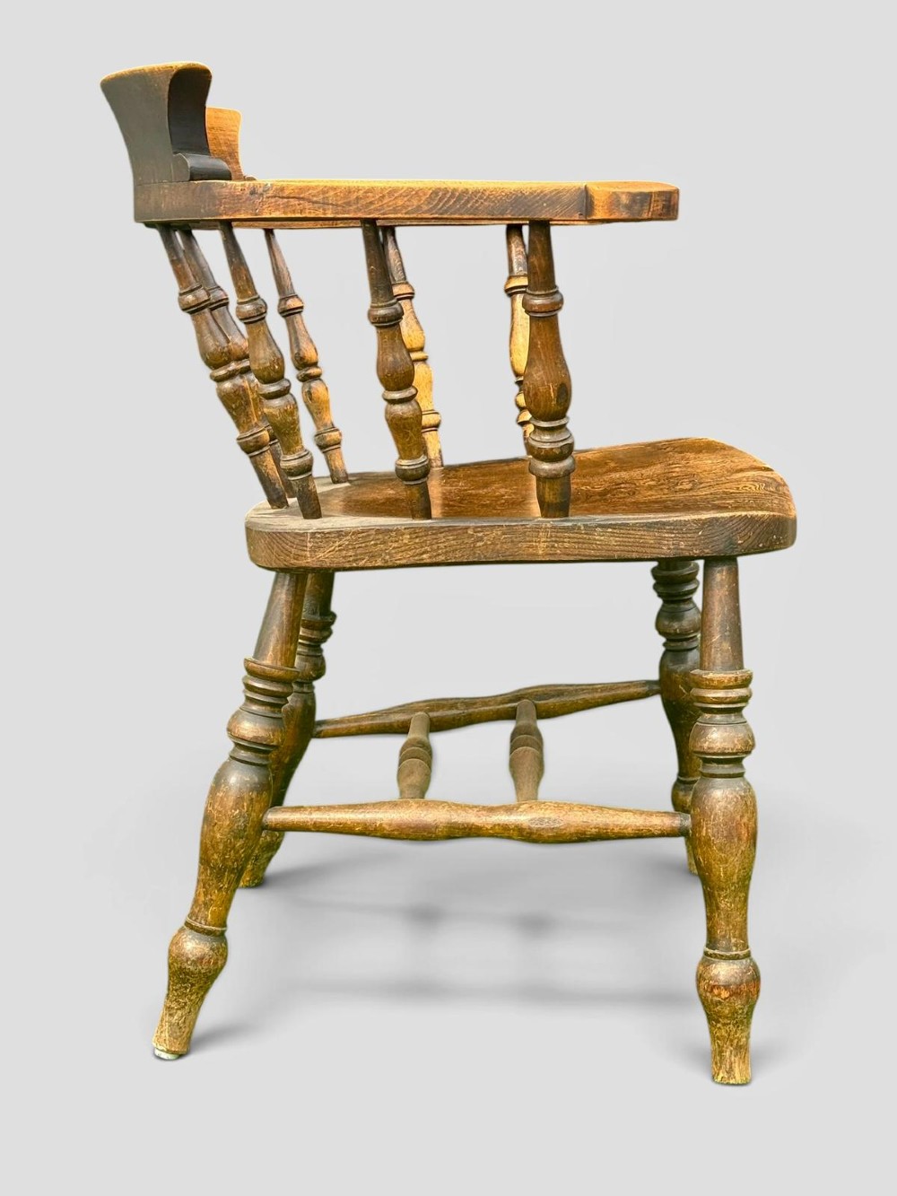 An antique Victorian beech and elm smokers captains chair with turned spindles, a contoured saddle seat, and turned legs. View V