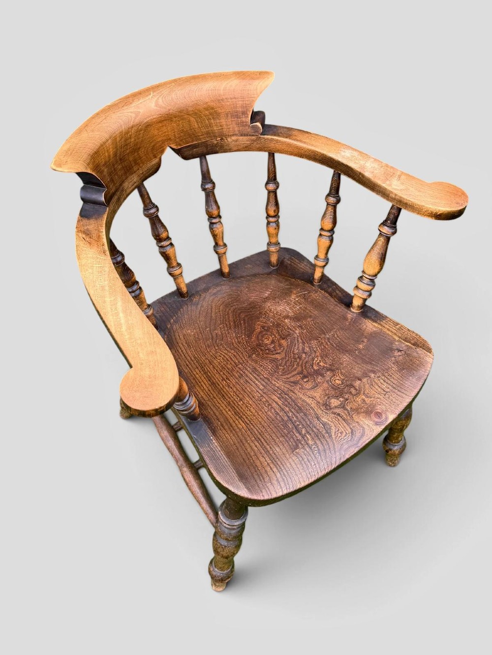 An antique Victorian beech and elm smokers captains chair with turned spindles, a contoured saddle seat, and turned legs. View VI