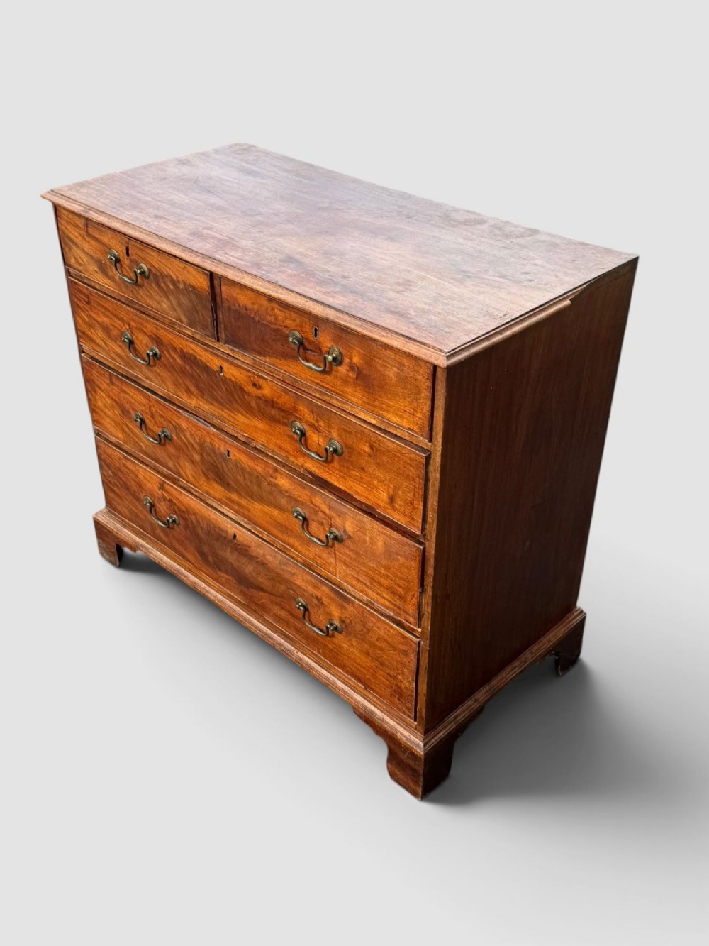 A Georgian mahogany chest of drawers featuring a two-over-three drawer configuration with brass swan-neck handles and bracket feet. View VI