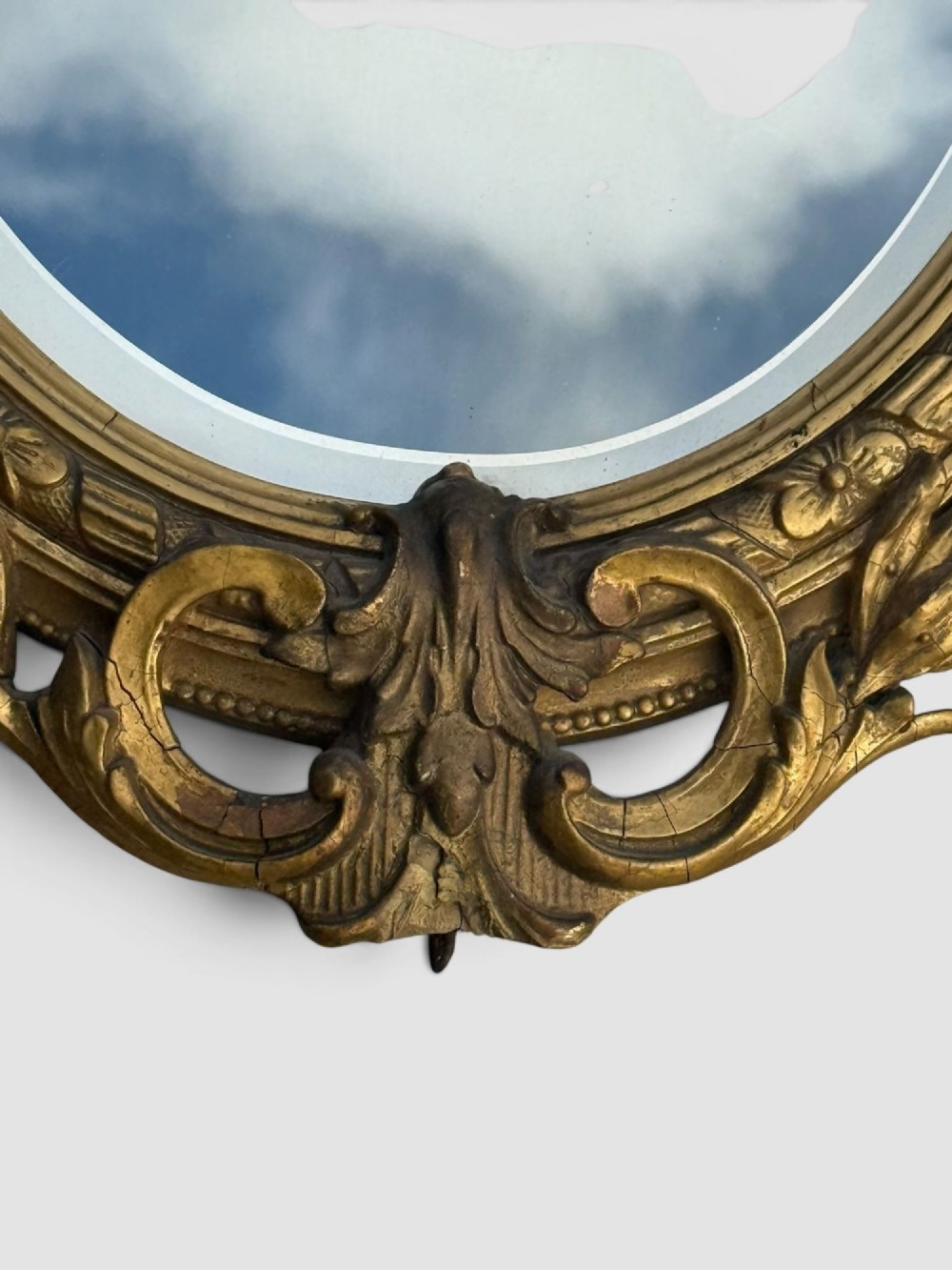 An oval Victorian gilt gesso wall mirror featuring an ornate floral crest, decorative scrollwork, and bevelled mirror glass. View V