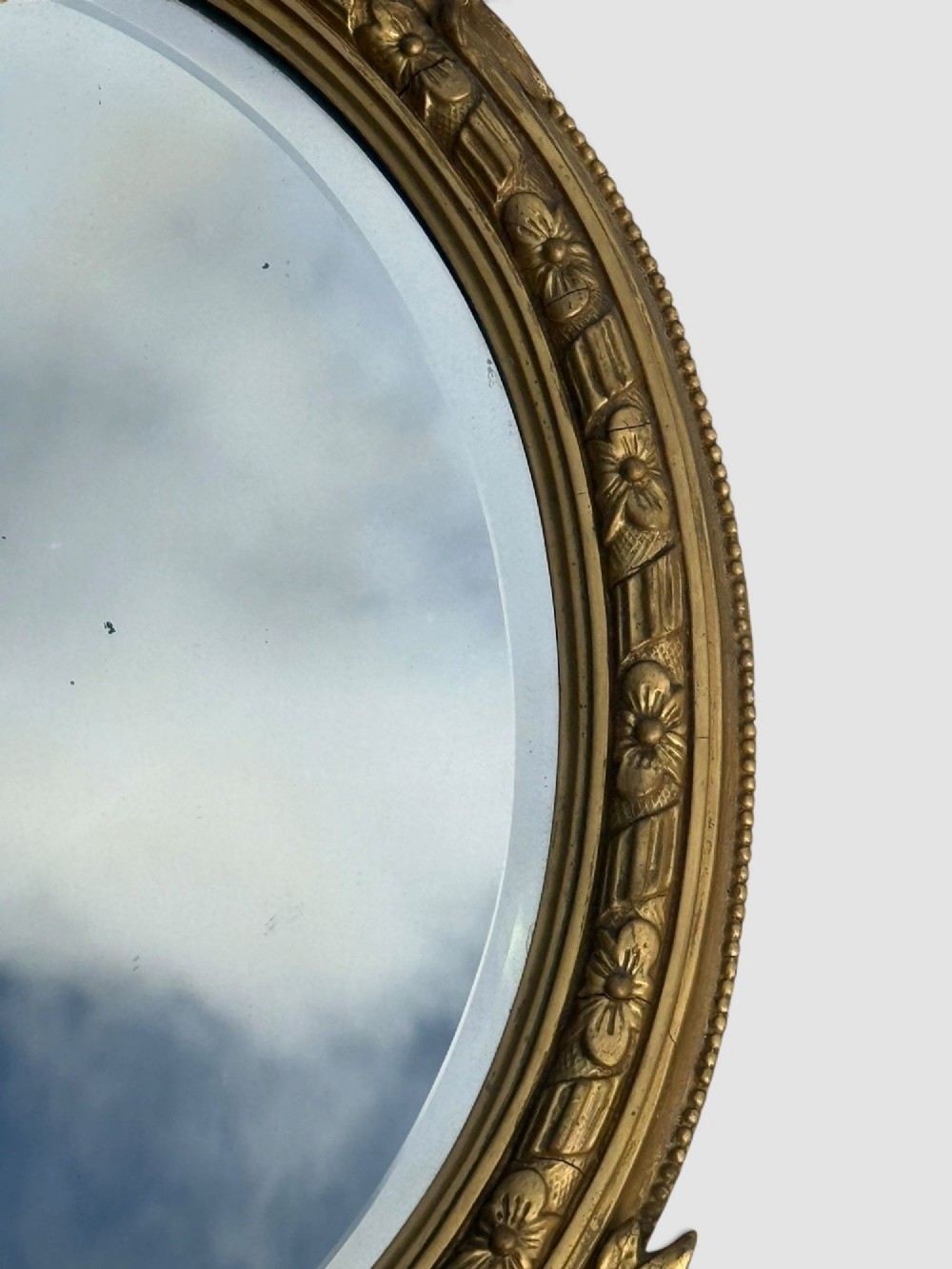 An oval Victorian gilt gesso wall mirror featuring an ornate floral crest, decorative scrollwork, and bevelled mirror glass. View VI