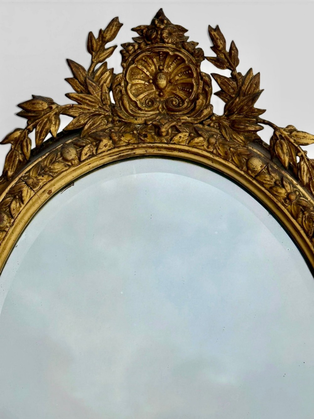 An oval Victorian giltwood and gesso girandole wall mirror featuring floral cresting, a beaded inner rim, and a three-branch candle sconce at the base. View II