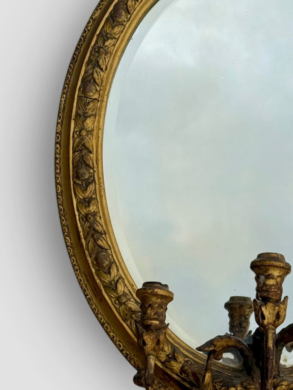 An oval Victorian giltwood and gesso girandole wall mirror featuring floral cresting, a beaded inner rim, and a three-branch candle sconce at the base. View III