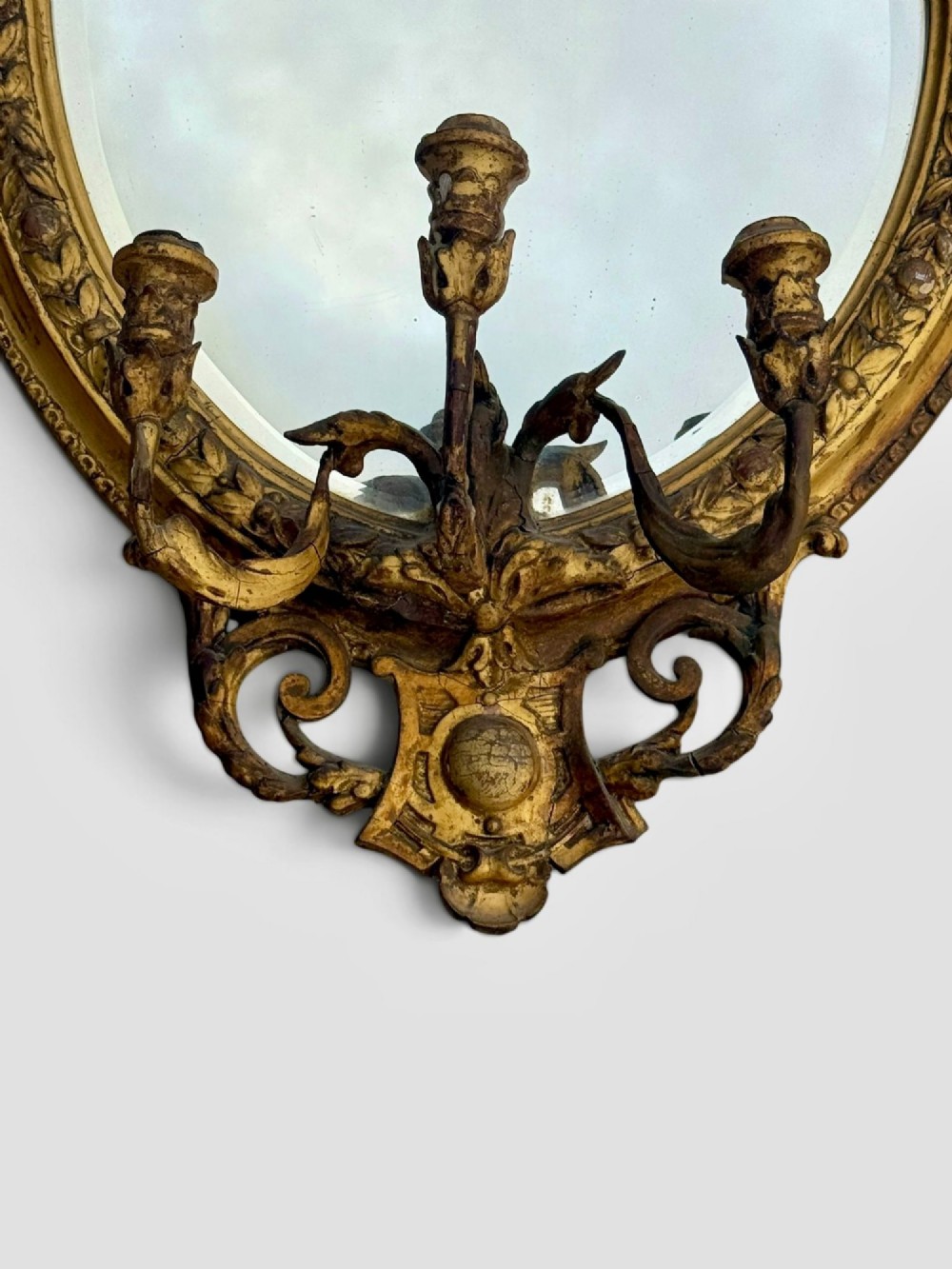 An oval Victorian giltwood and gesso girandole wall mirror featuring floral cresting, a beaded inner rim, and a three-branch candle sconce at the base. View IV
