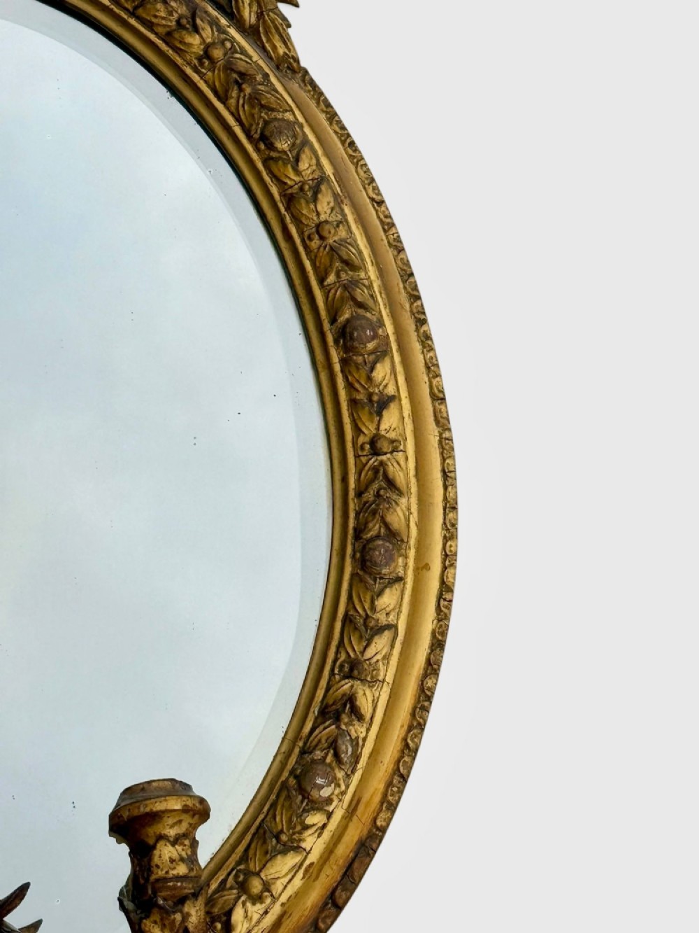 An oval Victorian giltwood and gesso girandole wall mirror featuring floral cresting, a beaded inner rim, and a three-branch candle sconce at the base. View V