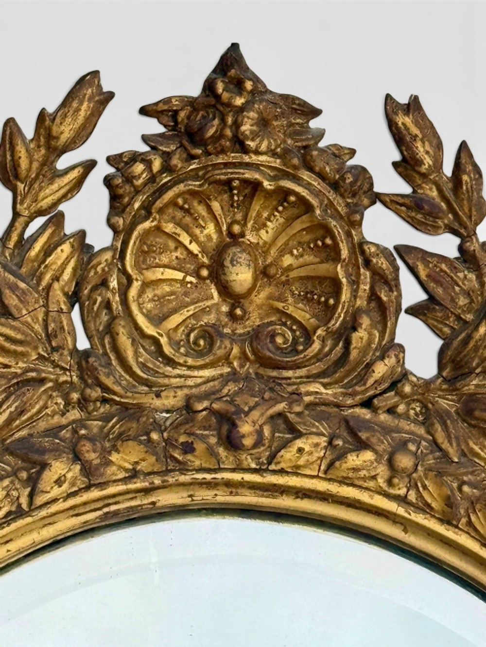 An oval Victorian giltwood and gesso girandole wall mirror featuring floral cresting, a beaded inner rim, and a three-branch candle sconce at the base. View VI