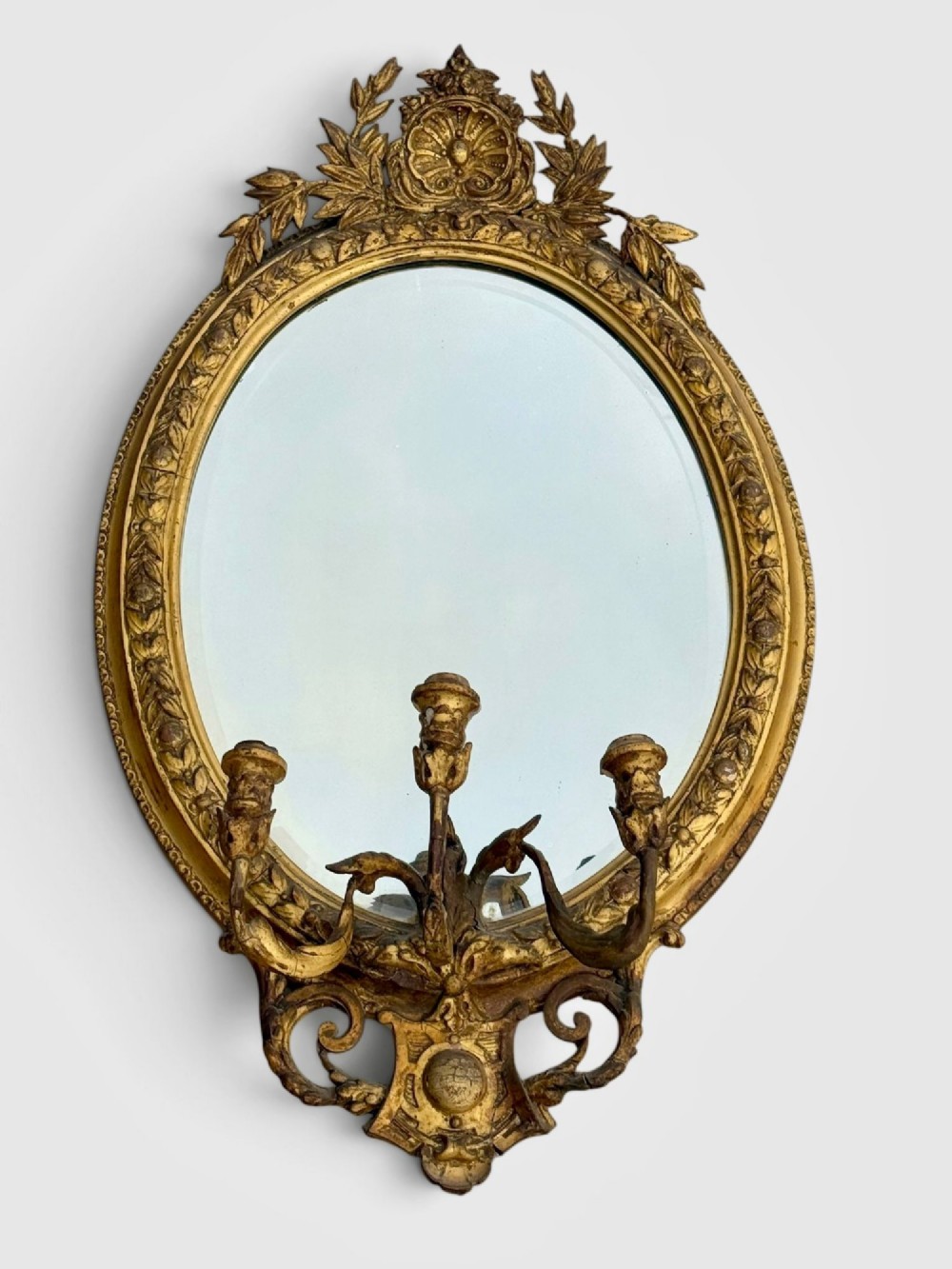 An oval Victorian giltwood and gesso girandole wall mirror featuring floral cresting, a beaded inner rim, and a three-branch candle sconce at the base. View VIII
